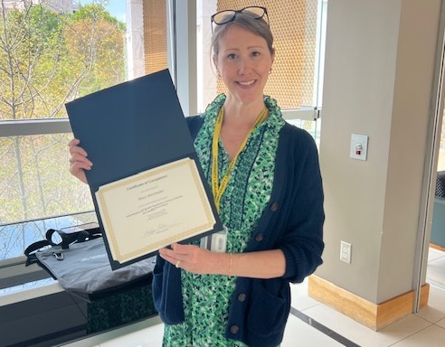Woman standing in hallway with windows holding a certificate.