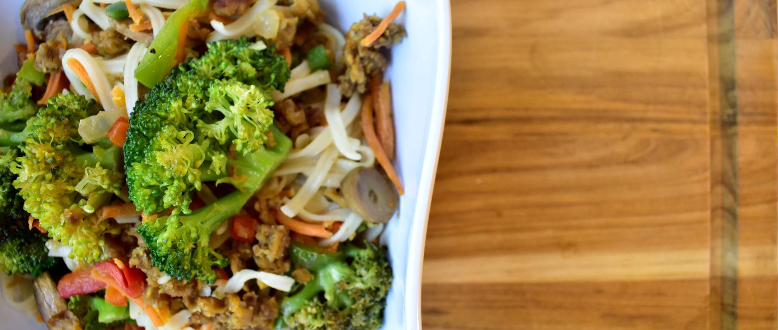 broccoli noodle bowl on wooden cutting board