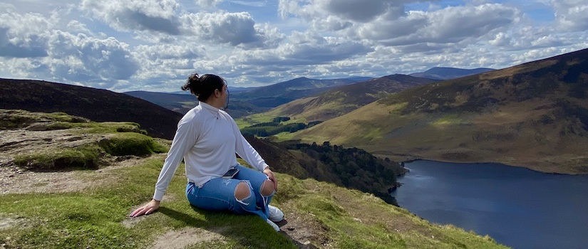 girl sitting on the grass on a mountain overlooking the view