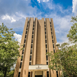 A side vantage point of Columbia Hall, that is flanked by green trees.