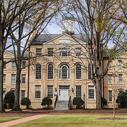 The wide green grass of the horseshoe in the foreground of Desaussure residence hall, with soon to bloom oak trees near the building.