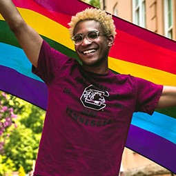 Student representing equality by holding a rainbow colored flag in the air. 