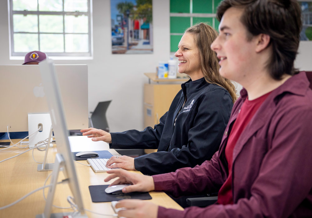 Students gathered around a computer discussing what is on the screen.
