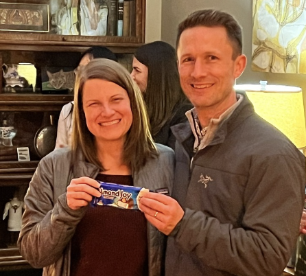 Kristy Welshhans, a white woman with short brown hair, and Rob Hock, a white man with cropped brown hair, pose with their "CANdies" award, an Almond Joy