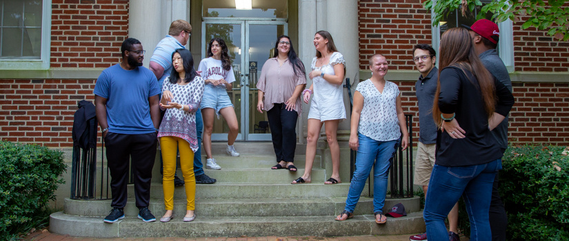 Eight students sitting around a table on the Russell House patio, an umbrella shading them from the sun