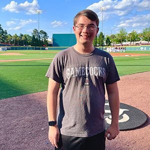 Student wearing a “Gamecocks” t-shirt, smiling while standing on a baseball field.