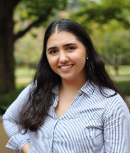 Mariajose wears a blue and white striped oxford and plaid skirt and smiles at the camera