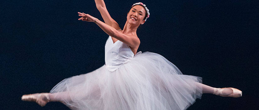 Female dancer performing on stage in grand jete. 