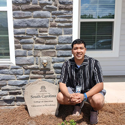 Juan Alvaredo outside of his house in the Teacher Village. A nearby plaque reads "University of South Carolina College of Education Educators in Residence"