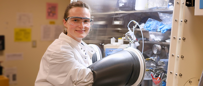 Female student looking at camera with her hands in a glove, working in a pressure box.