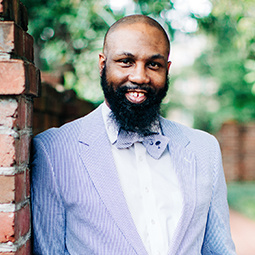 Man with a beard smiling, wearing a white and light blue suit with matching blue bow tie