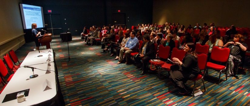 Professor standing at a podium giving a presentation to an audience of 50 or more