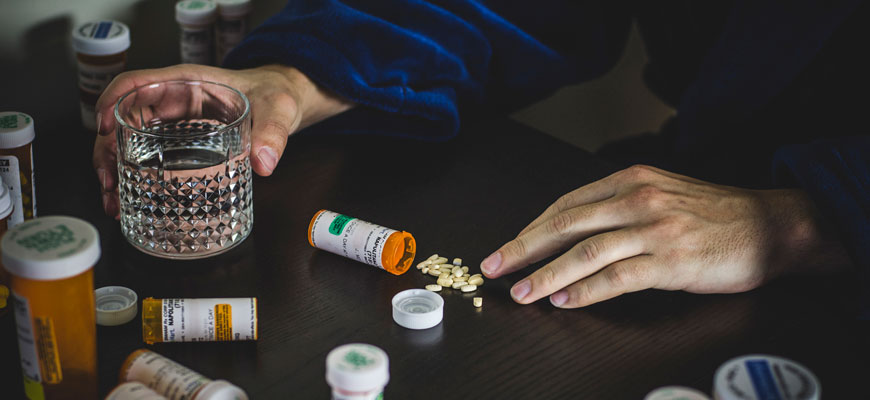 Man holding glass of water with prescription pills on table next to him