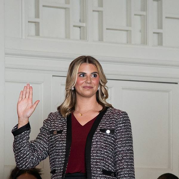 woman stands with her right hand raised