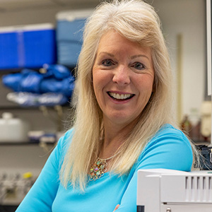 Casual head shot of blonde woman in blue sweater in laboratory setting