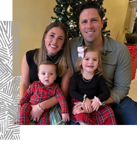 two people hold two children in front of a christmas tree